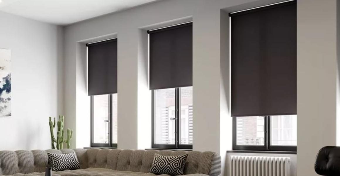 Living room with black roller blinds on multiple windows, neutral grey walls, and a modern sofa with patterned cushions.